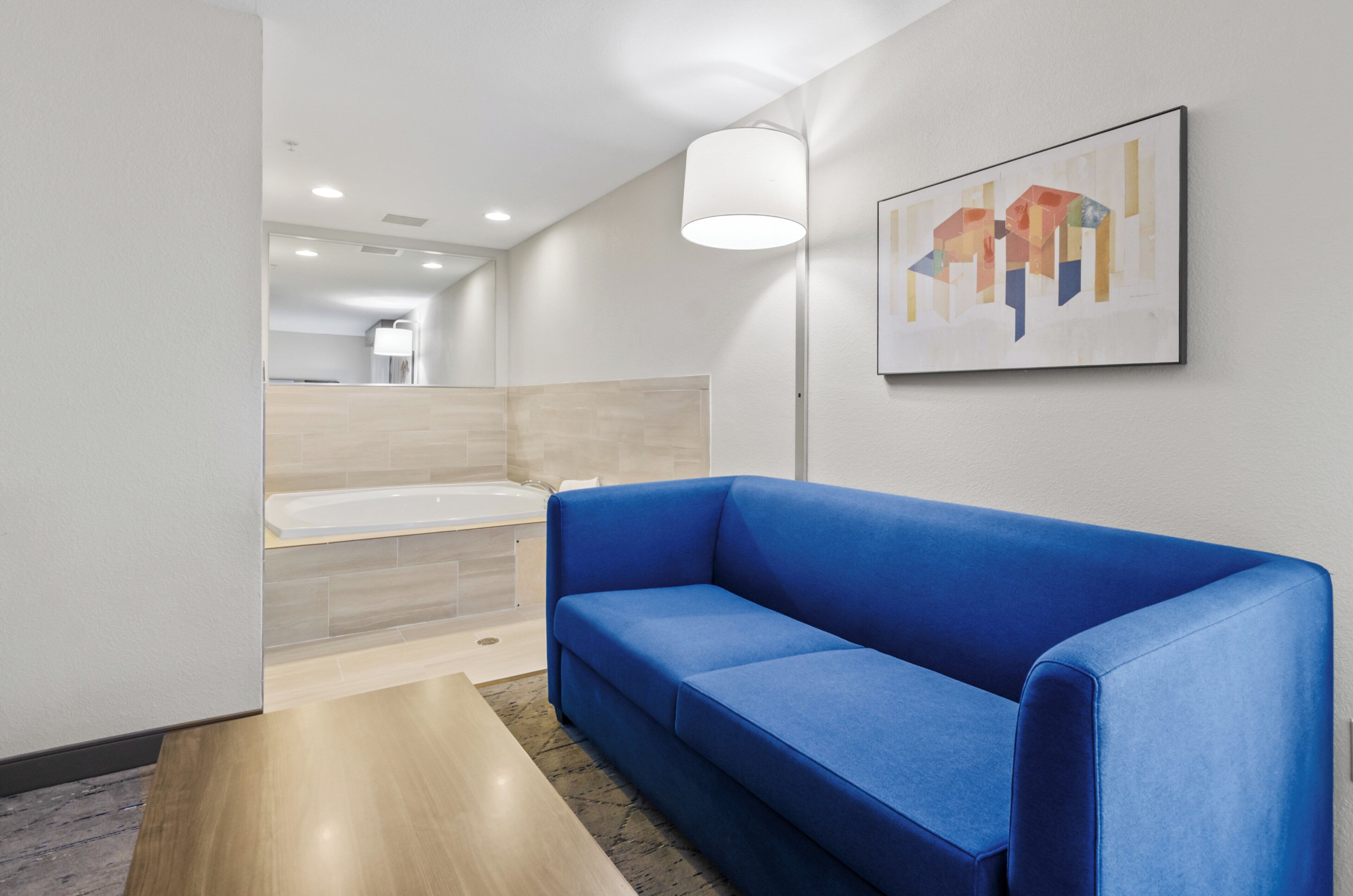 A modern bathroom with a bathtub, a blue sofa, and a wall-mounted abstract painting.
