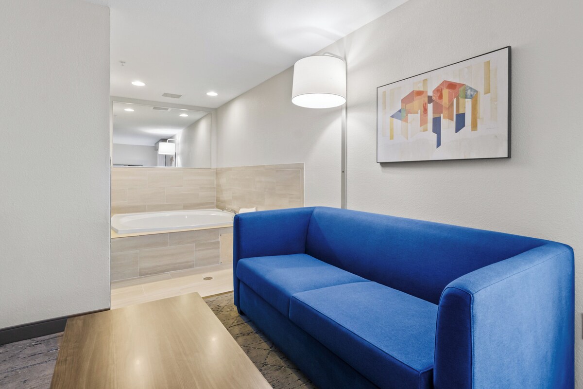 A modern bathroom with a bathtub, a blue sofa, and a wall-mounted abstract painting.