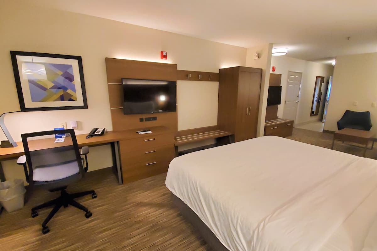 A hotel room with a bed, a desk with a computer, a chair, a television, and a wardrobe.