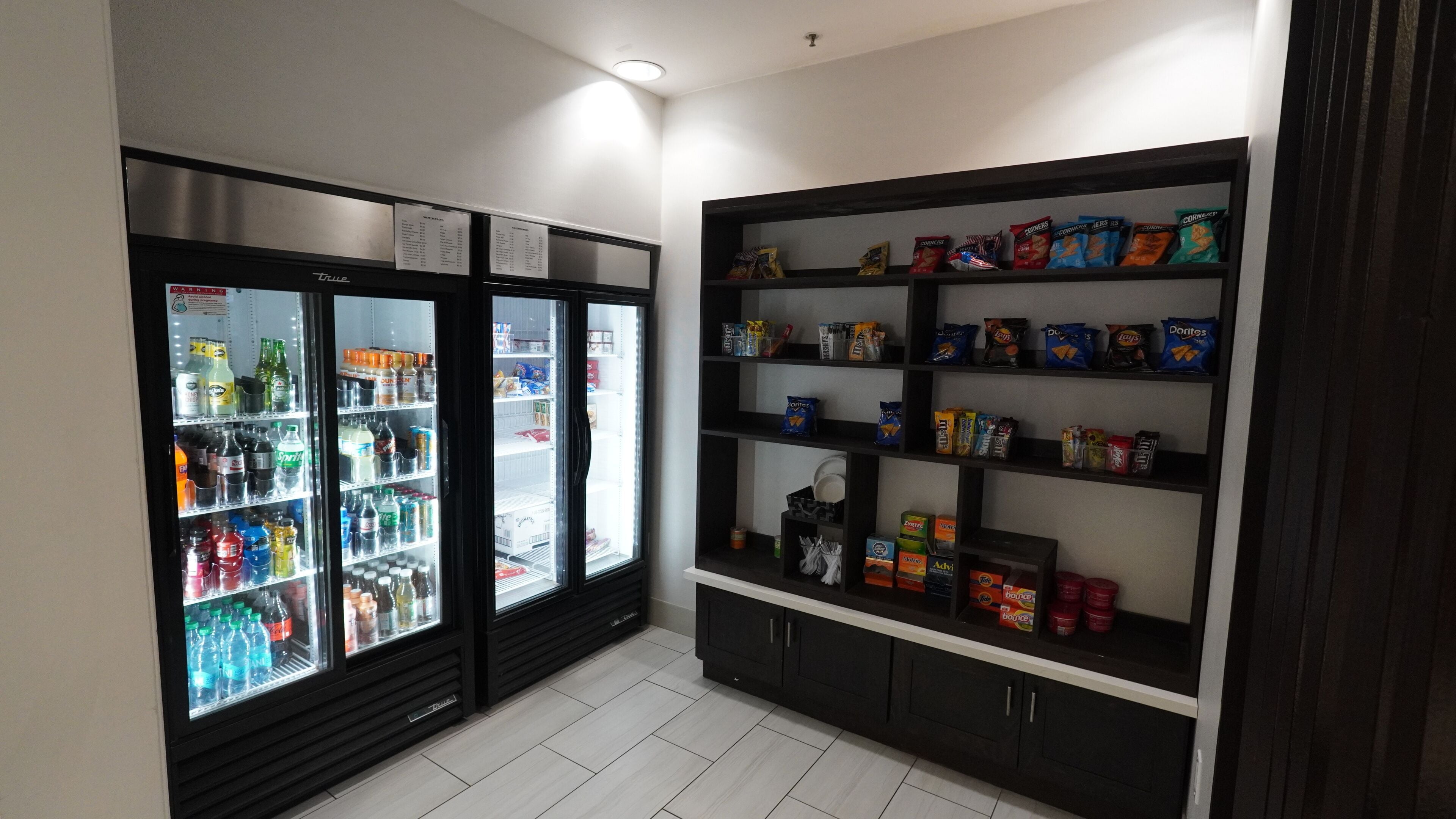 Uma área de vending com duas geladeiras repletas de bebidas e prateleiras com lanches.