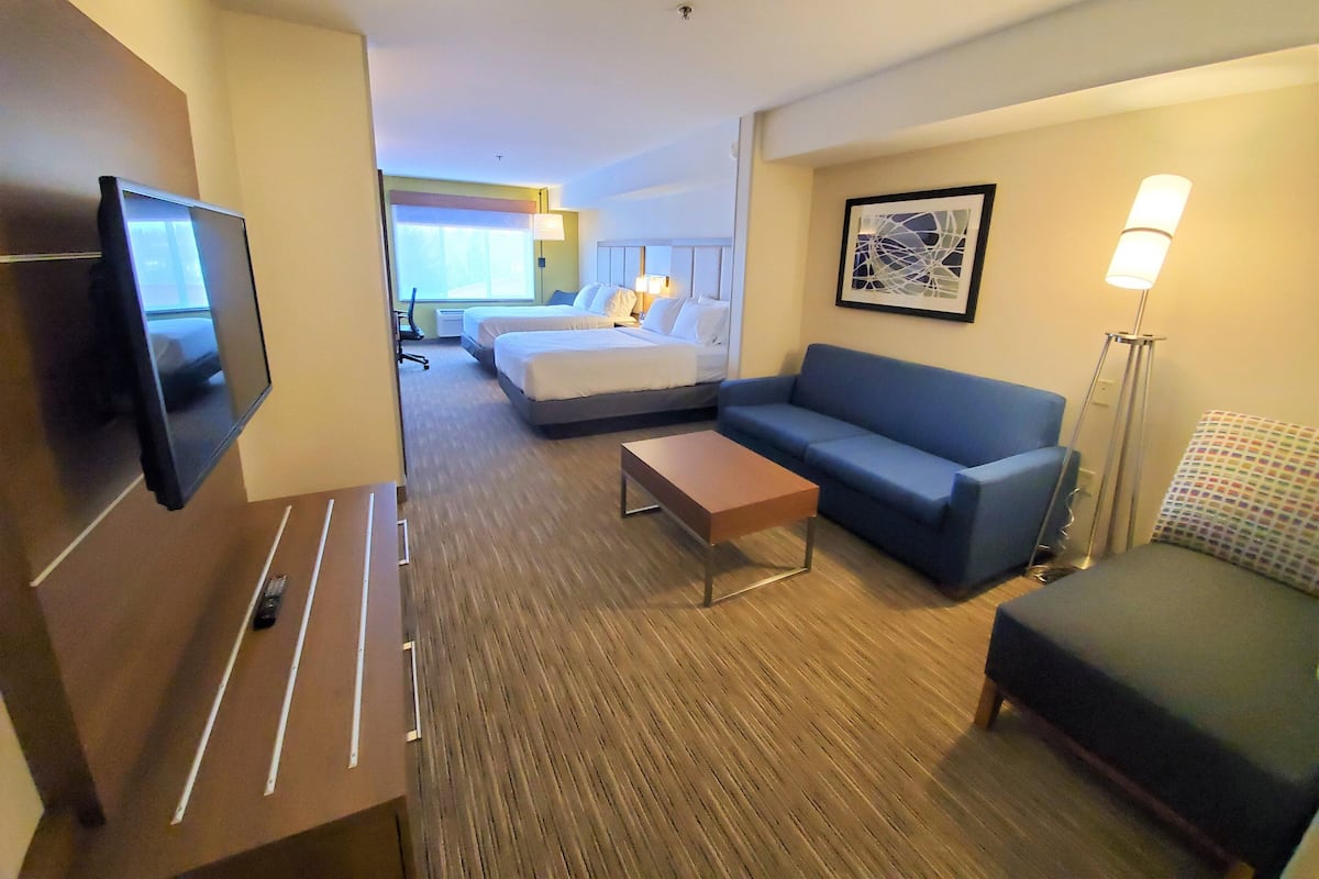A hotel room with a TV, a sofa, a bed, a desk, and a lamp.