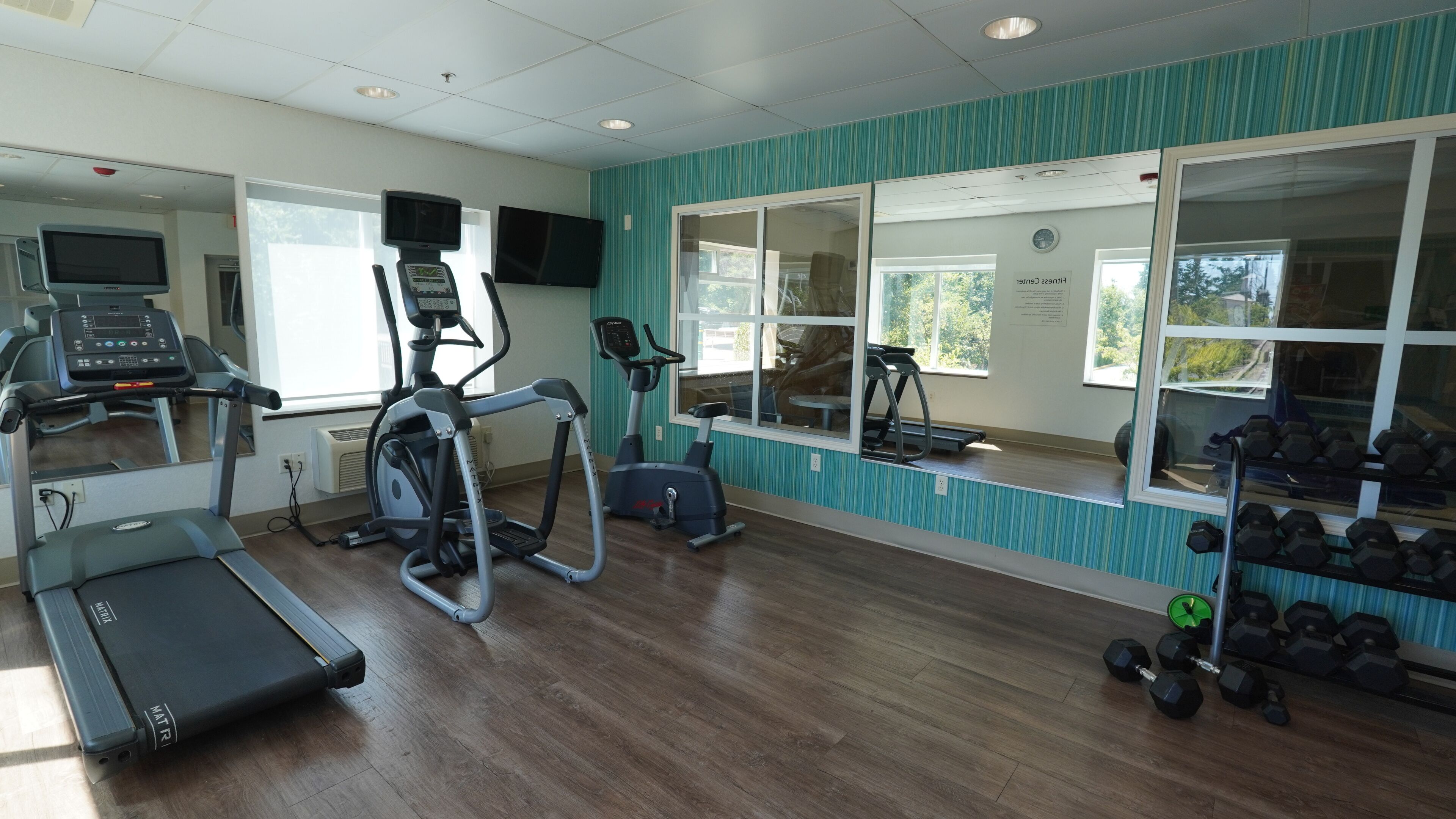A gym with treadmills, an elliptical, and a mirror wall.