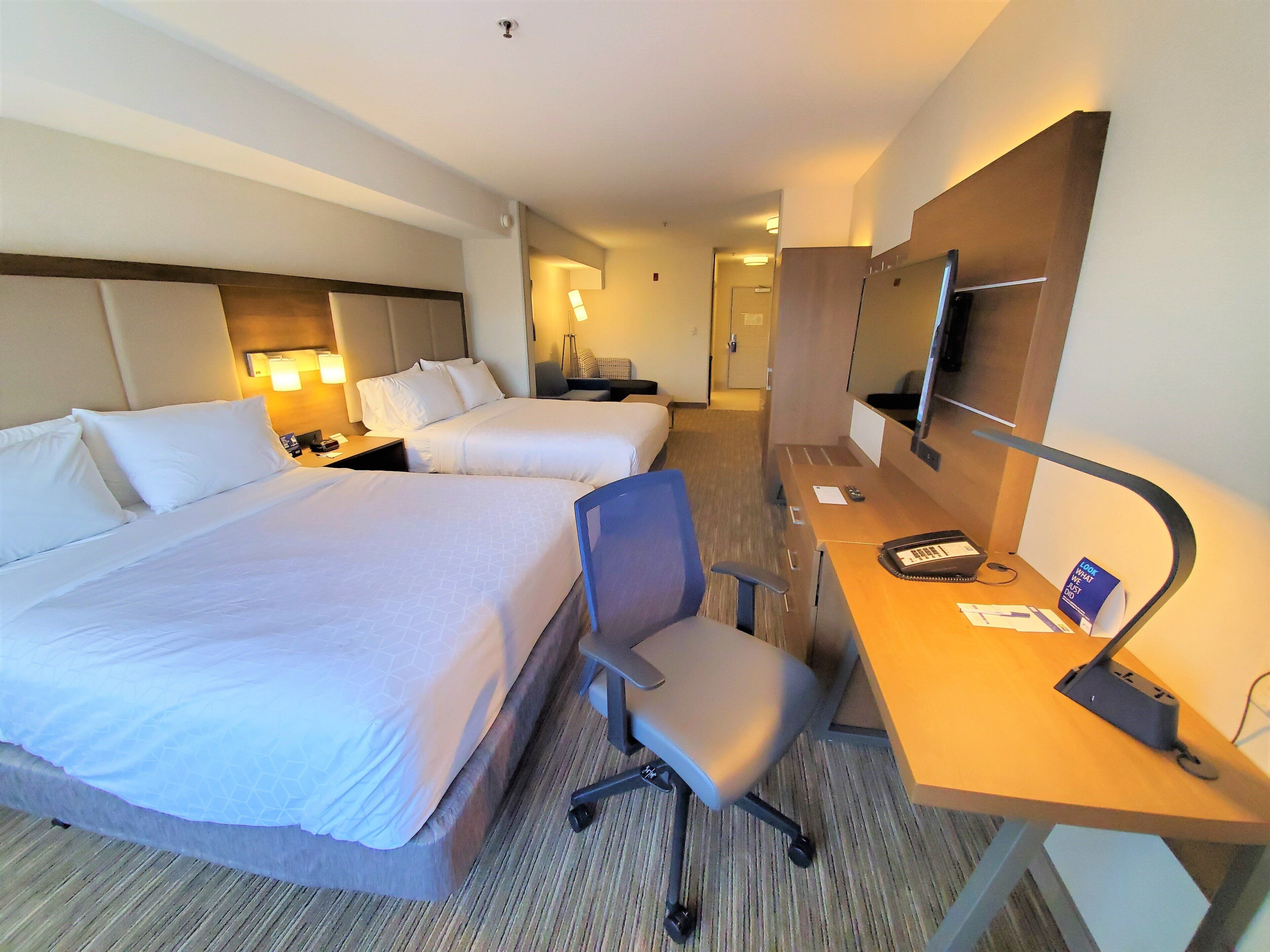 A hotel room with two beds, a desk with a computer, a chair, and a TV.