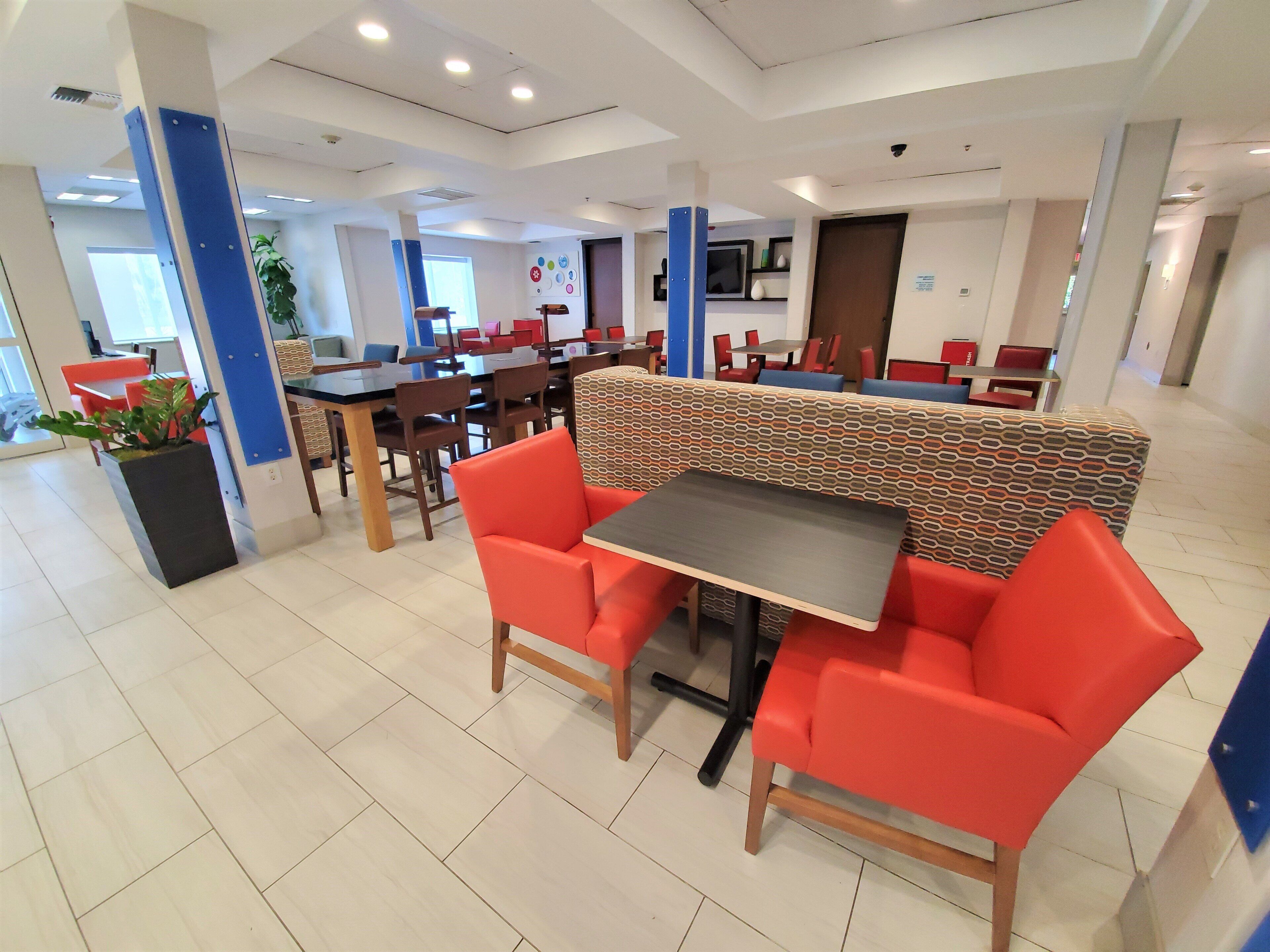 Un área de comedor interior moderna con cabinas y mesas, una pared con estampado y una planta en maceta.
