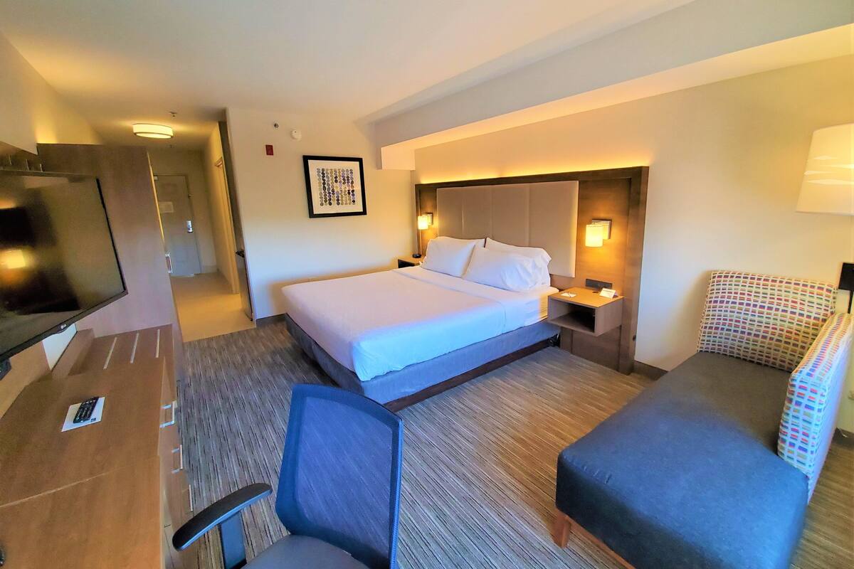 A hotel room with a bed, a desk, a chair, a TV, and a bedside table.