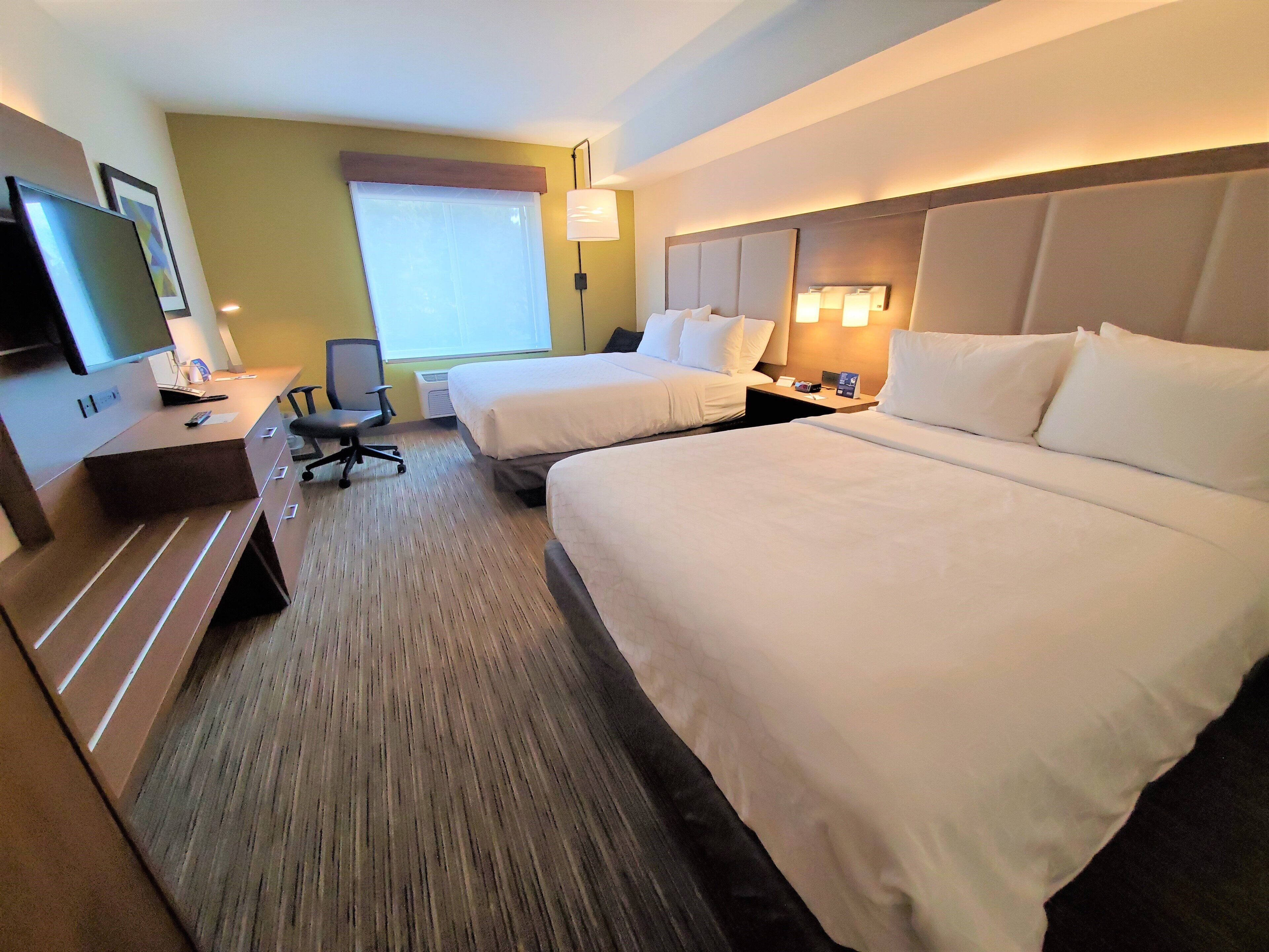 Quarto de hotel com duas camas, uma escrivaninha, uma cadeira, uma televisão e uma janela.