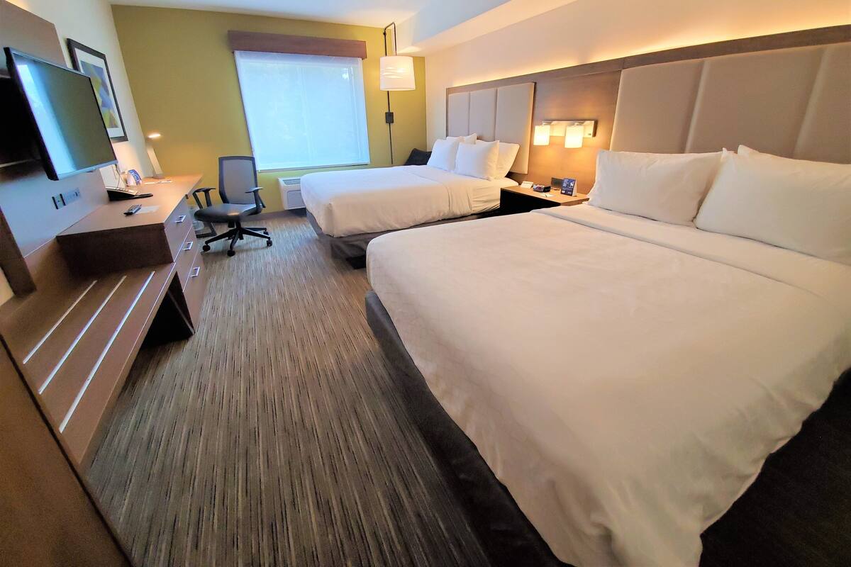 A hotel room with two beds, a desk, a chair, a TV, and a window with curtains.