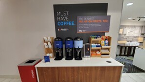 A coffee station with multiple coffee dispensers, a trash bin, and a sign promoting a rewards club. - Holiday Inn Express & Suites Seattle North - Lynnwood by IHG (Lynnwood)