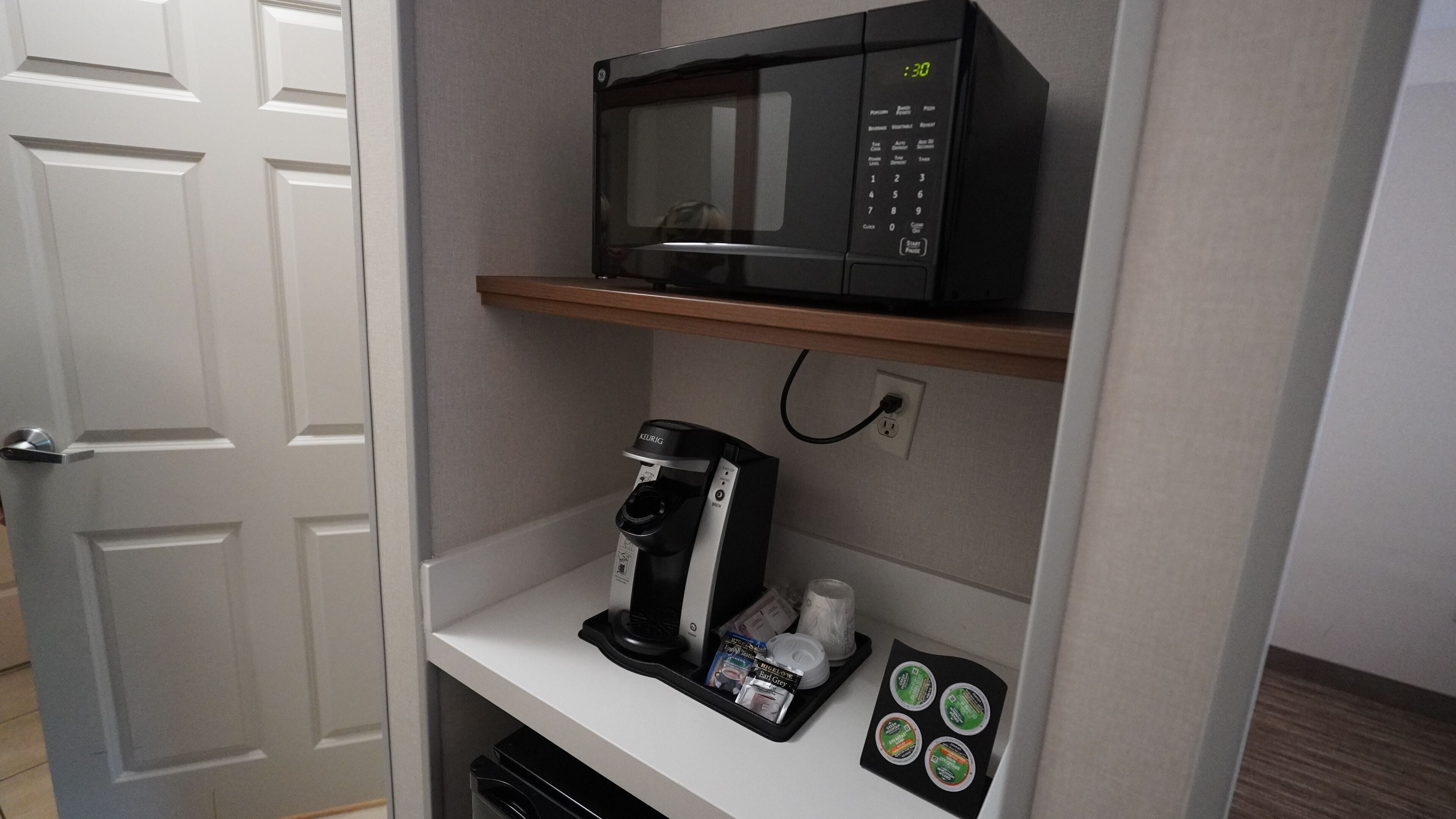A kitchenette with a microwave, coffee maker, and a shelf with coffee pods.