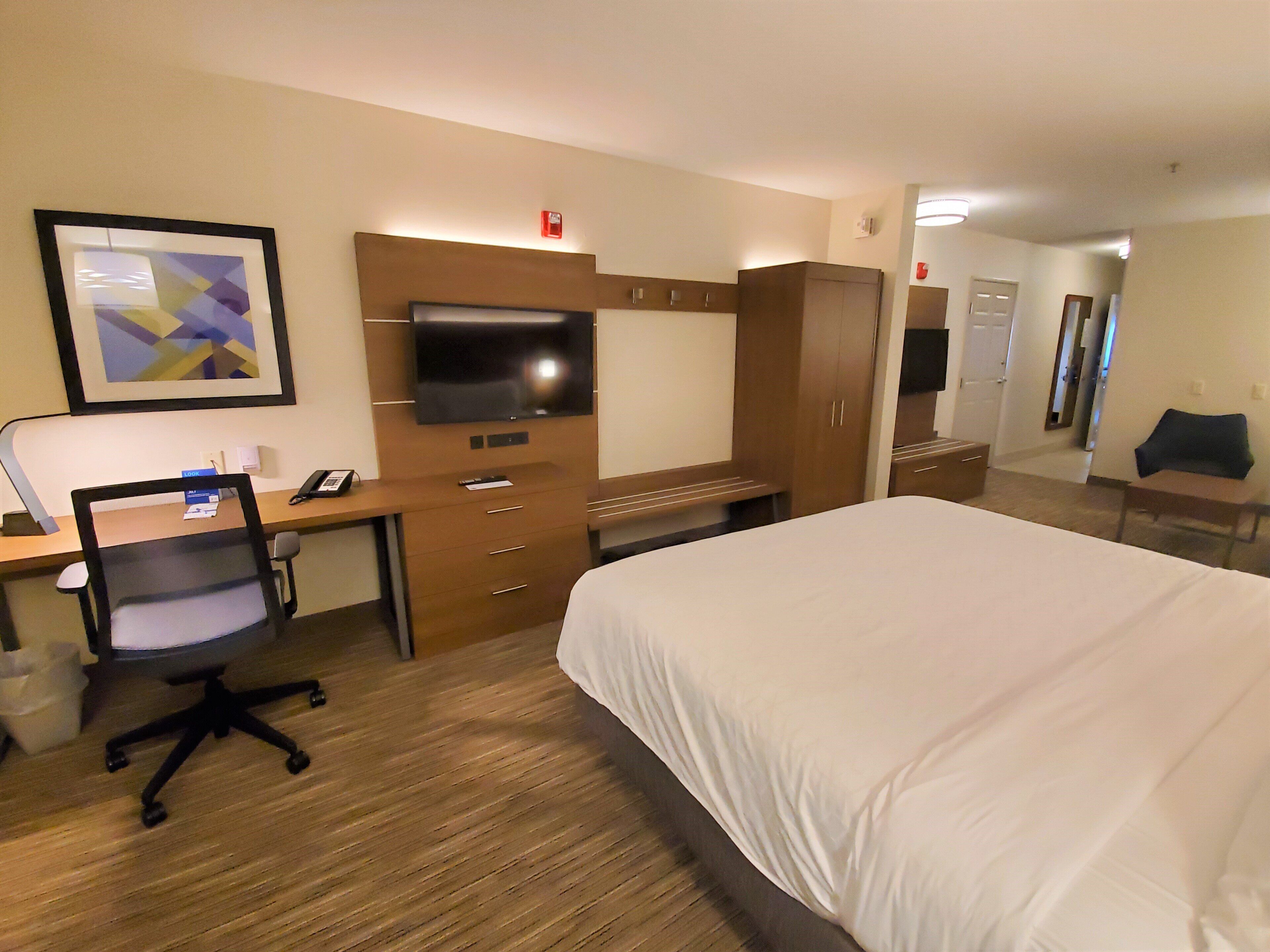 Habitación de hotel con cama, escritorio, silla, televisor, armario y un cuadro en la pared.