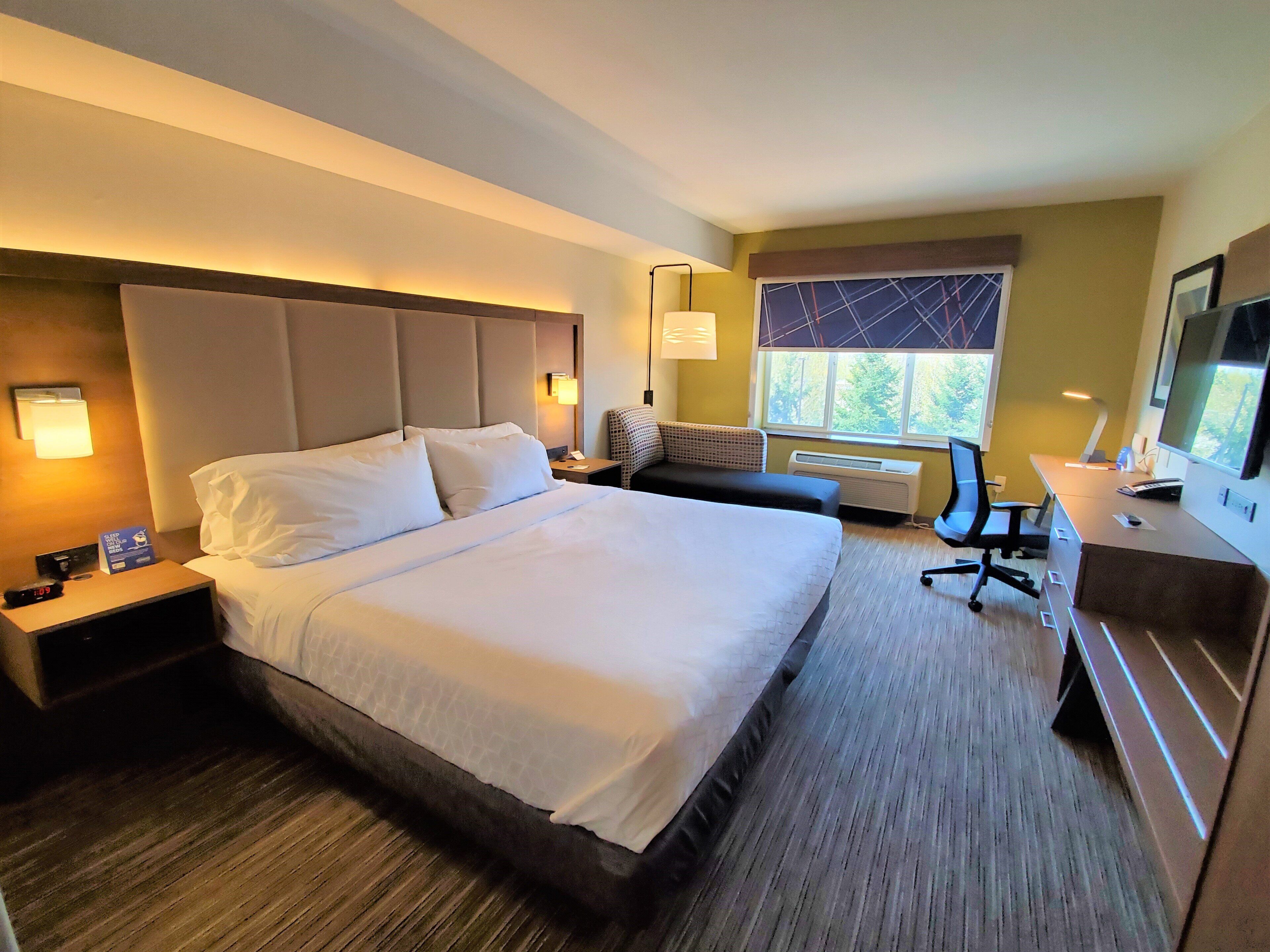 A hotel room with a large bed, bedside tables, a desk, a chair, and a television.