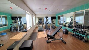 Un gimnasio con cintas de correr, elípticas, una banca y un estante con mancuernas.