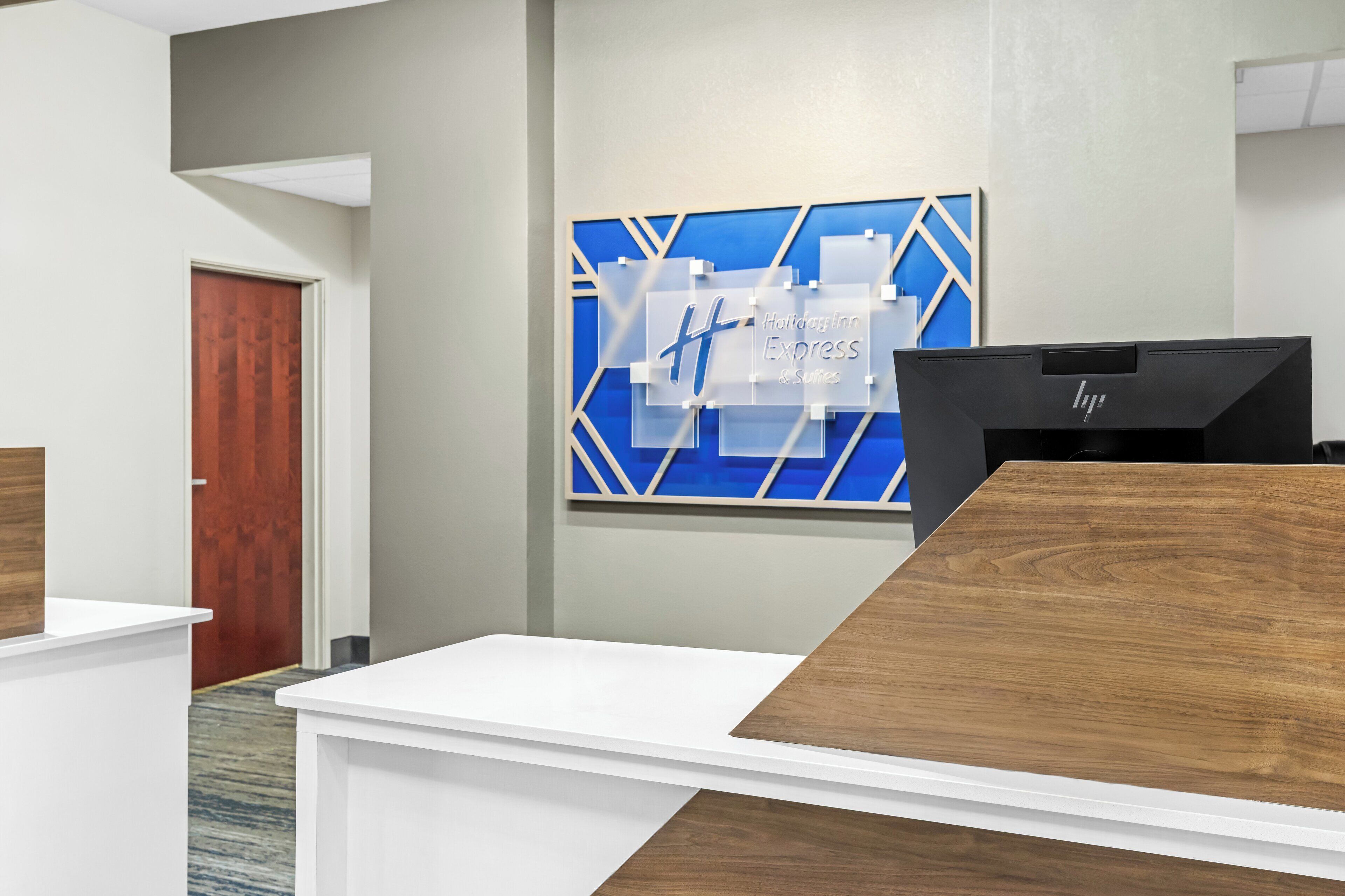 A reception area with a modern design, featuring a blue and white geometric wall art, a wooden reception desk, and a HP computer.