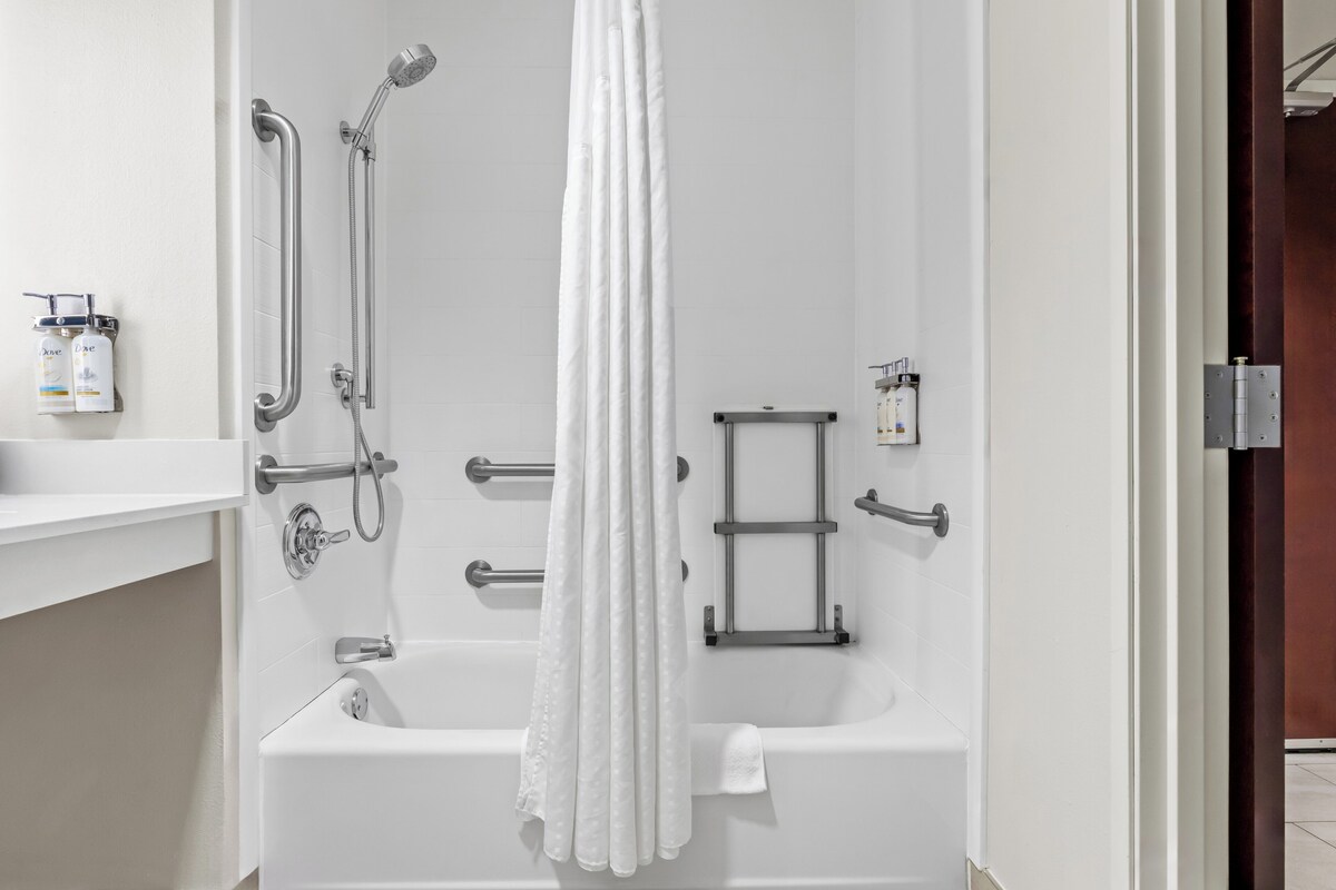 Une salle de bain moderne avec une baignoire blanche, des barres d’appui, une pomme de douche et un porte-serviettes.