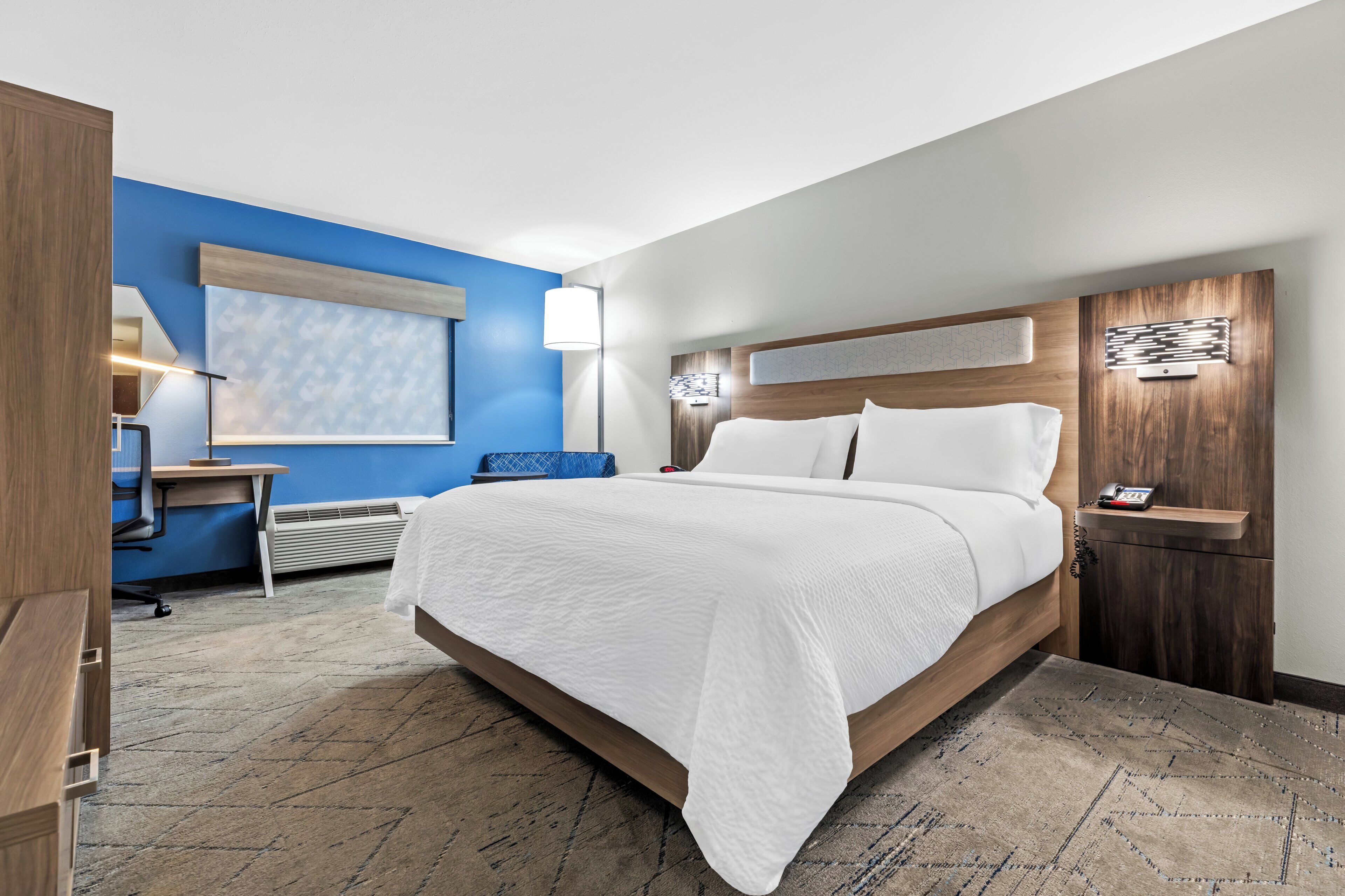Une chambre d’hôtel avec un grand lit, un bureau avec une chaise, un mur d’accent bleu et une tête de lit moderne.