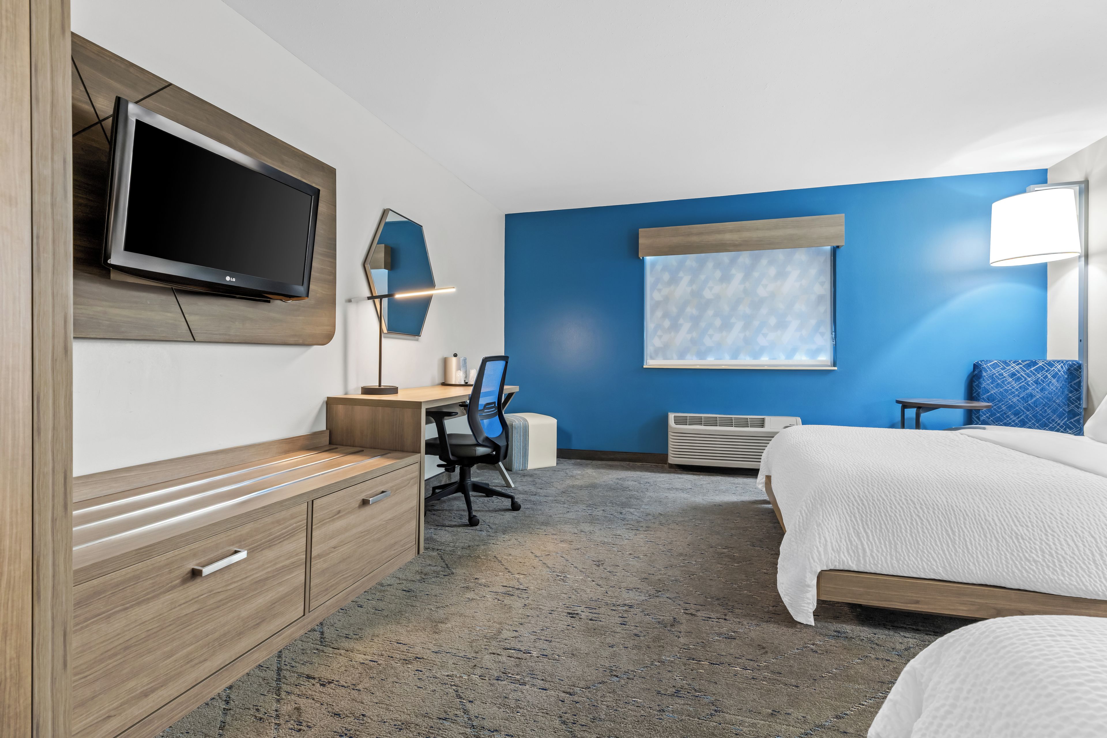 A hotel room with a bed, desk, chair, TV, and a window with blinds.