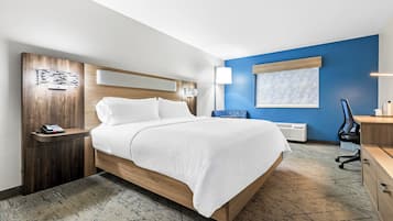 Habitación de hotel con cama, mesita de noche con teléfono, escritorio y silla, y ventana con persianas.
