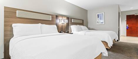 A hotel room with two beds, a wooden headboard, a wall-mounted light fixture, and a framed picture.