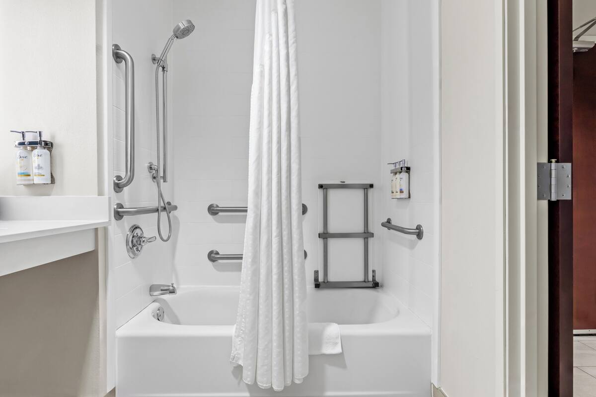 A modern bathroom with a bathtub, shower, grab bars, and a towel rack.