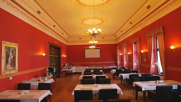 A banquet hall with tables set for dining, a chandelier, and a large painting on the wall.