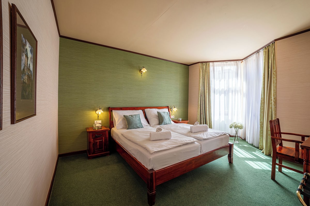 A neatly made double bed with pillows, a bedside table with a lamp, and a chair in a corner.