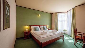 A neatly made double bed with pillows, a bedside table with a lamp, and a chair in a corner.