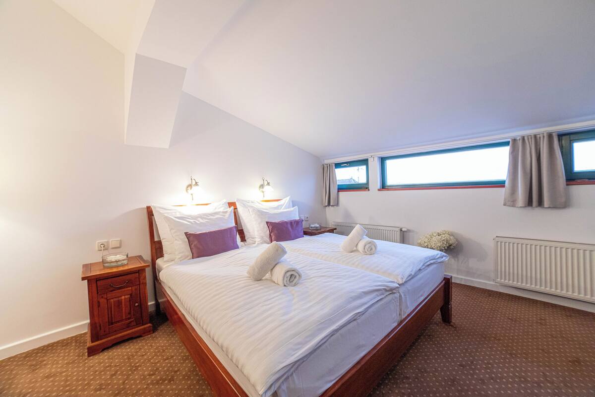 A bedroom with a large bed, two bedside tables, a window with curtains, and a radiator.