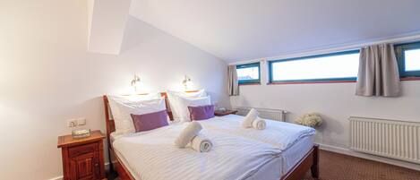 A bedroom with a large bed, two bedside tables, a window with curtains, and a radiator.