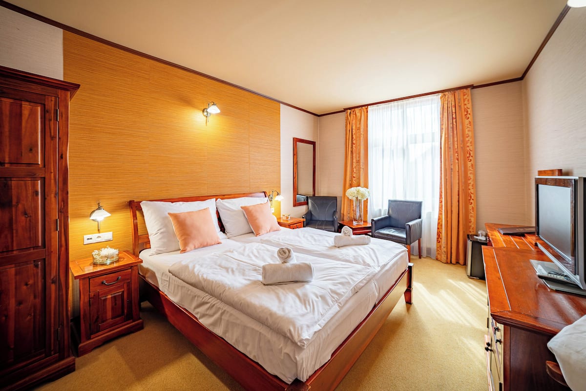 A hotel room with a large bed, a desk with a computer, a chair, a wardrobe, and a television.