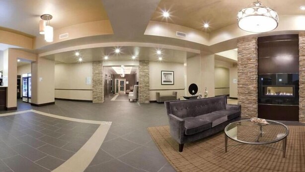 A spacious lobby with a grey sofa, a glass coffee table, and a stone accent wall with a fireplace. - Holiday Inn Express Hotel & Suites PORT ARTHUR by IHG (Port Arthur)