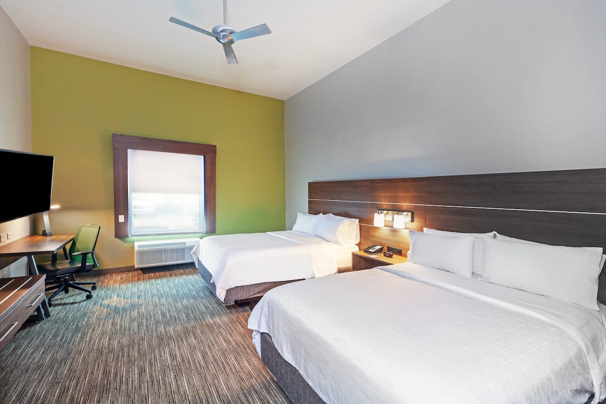 A hotel room with two beds, a desk, a chair, a television, and a ceiling fan.