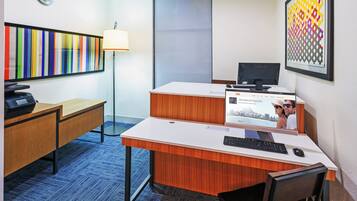 A hotel room with a desk, chair, computer, printer, lamp, and a large window.