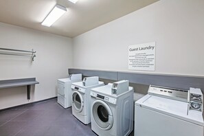 A guest laundry area with a sign, two front-loading washers, and a dryer. - Holiday Inn Express Hotel & Suites PORT ARTHUR by IHG (Port Arthur)
