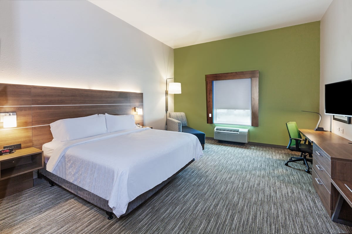 A hotel room with a large bed, bedside tables, a desk with a chair, a television, and a window with blinds.