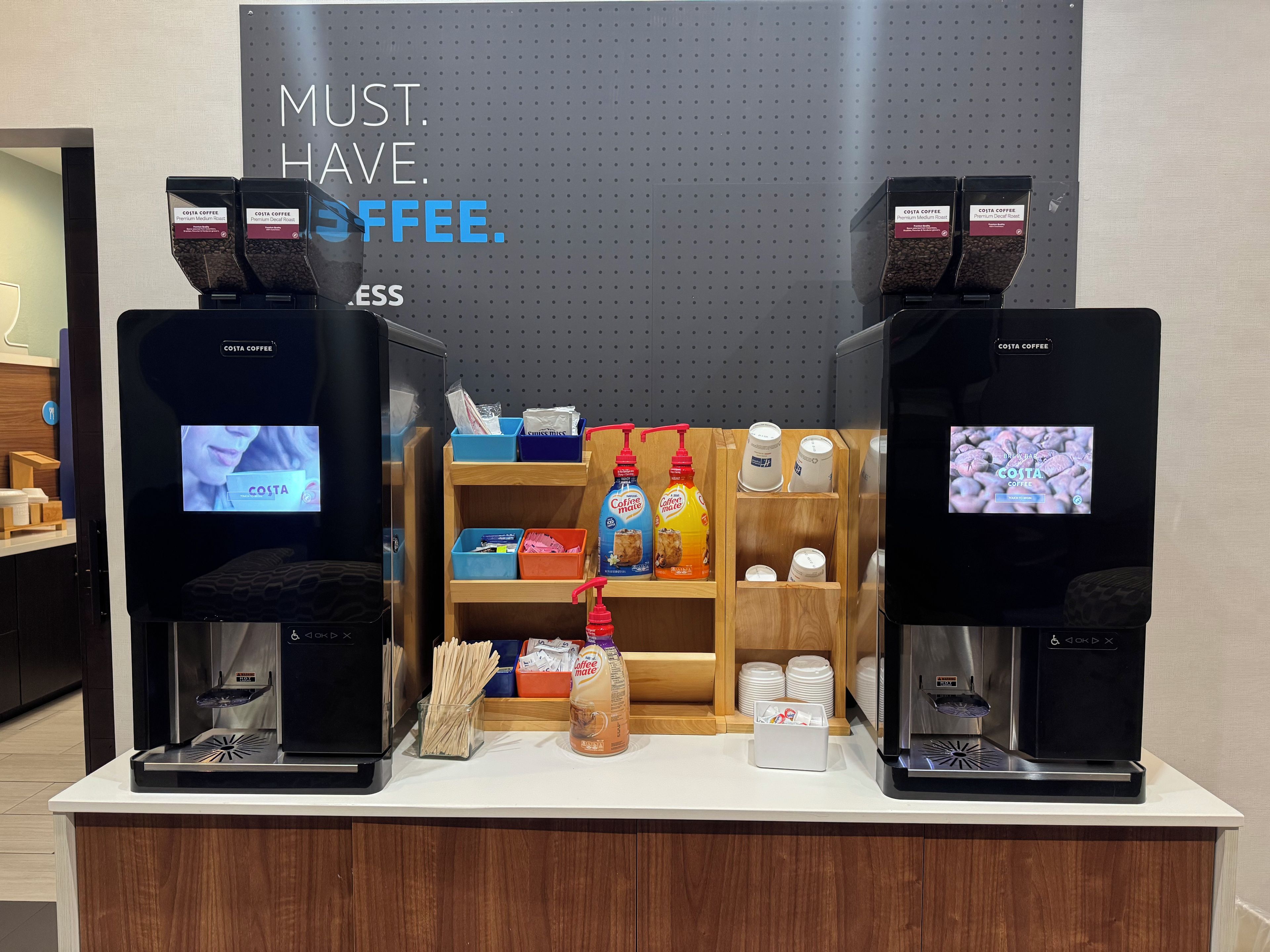 A coffee station with two coffee dispensers, a sign that reads 'MUST. HAVE. COFFEE.', and various coffee-related items on display.