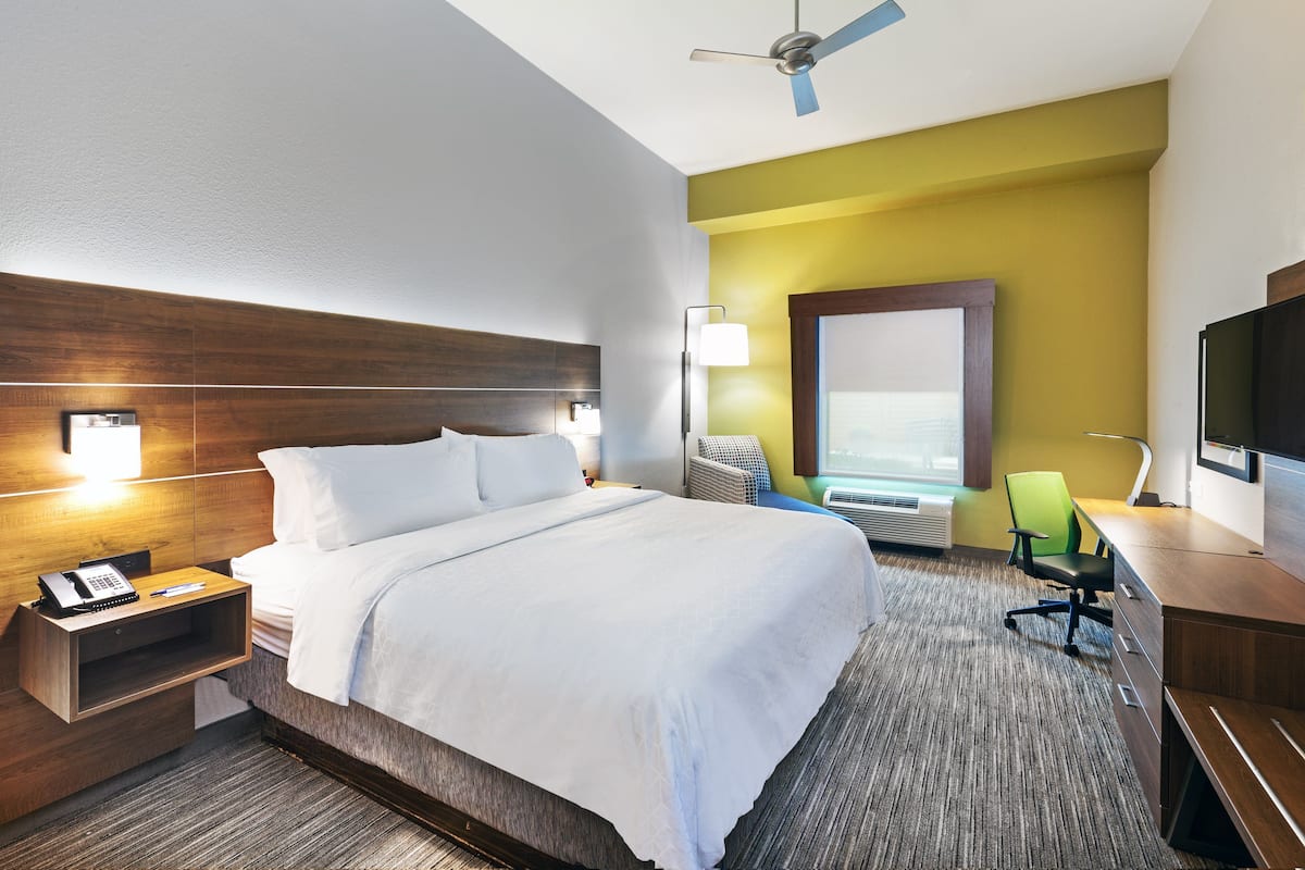 A hotel room with a large bed, a desk, a chair, a television, and a ceiling fan.