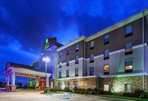 Hotel building with a flat roof and multiple floors, surrounded by a lawn and parking area.