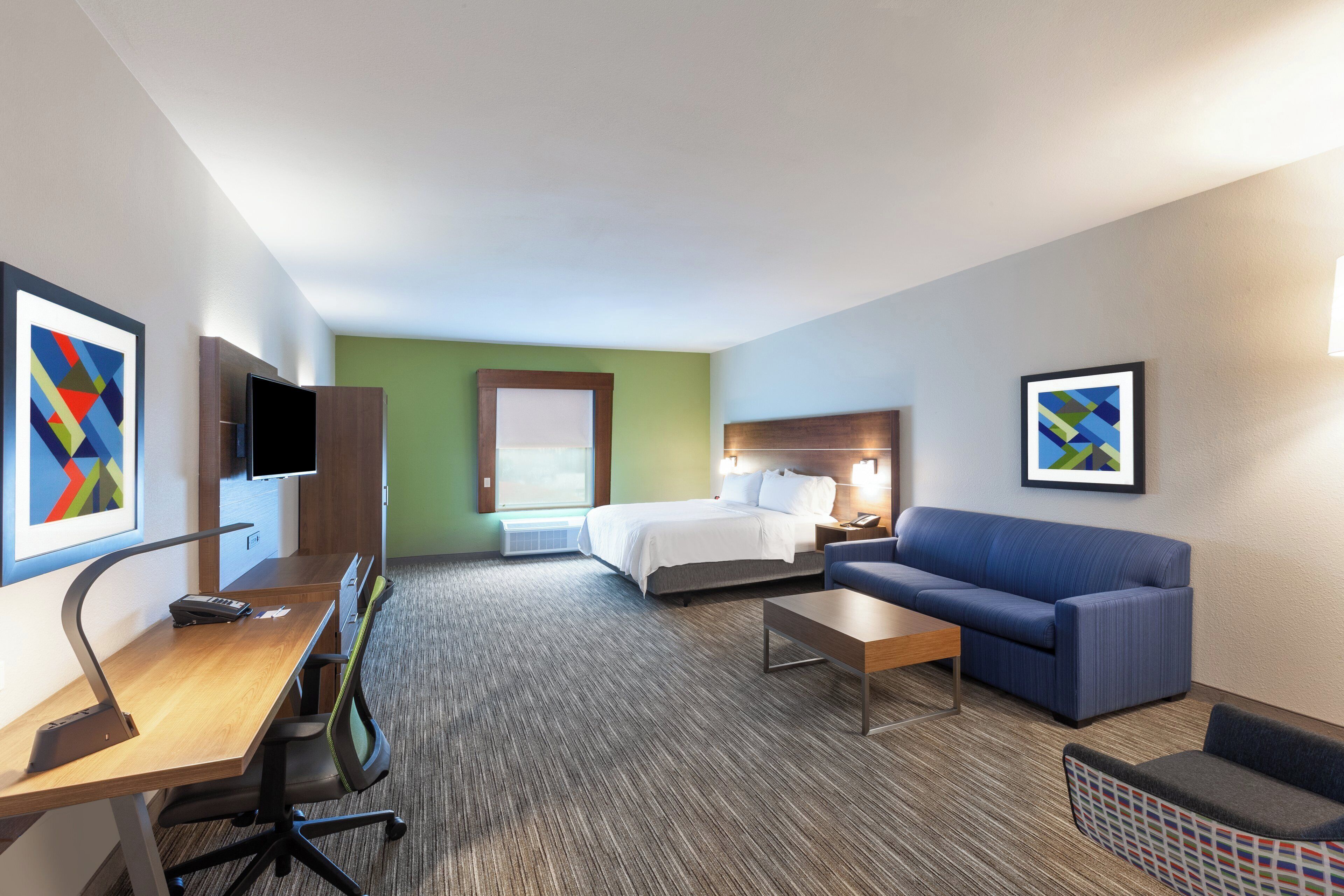 Une chambre d’hôtel équipée d’un lit, d’un bureau, d’une chaise, d’un canapé et d’une télévision.