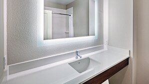 A bathroom with a white sink, a mirror with a lighted frame, and a shower visible in the reflection. - Holiday Inn Express Hotel & Suites PORT ARTHUR by IHG (Port Arthur)