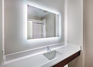 A bathroom with a white sink, a mirror with a lighted frame, and a shower visible in the reflection. - Holiday Inn Express Hotel & Suites PORT ARTHUR by IHG (Port Arthur)