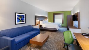 A hotel room with a bed, a blue sofa, a wooden table, a green chair, a TV, and a framed picture on the wall. - Holiday Inn Express Hotel & Suites PORT ARTHUR by IHG (Port Arthur)