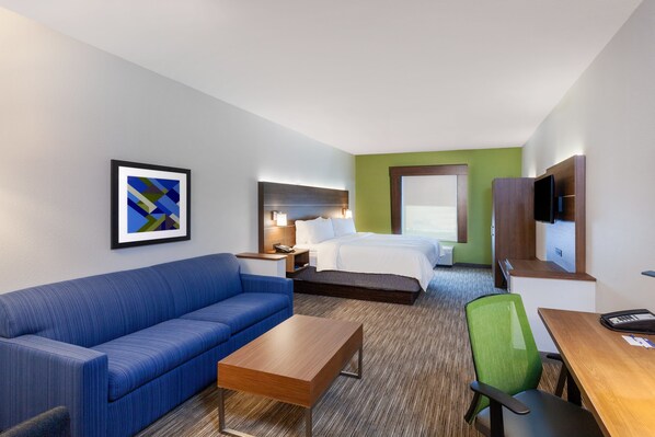 A hotel room with a bed, a blue sofa, a wooden table, a green chair, a TV, and a framed picture on the wall. - Holiday Inn Express Hotel & Suites PORT ARTHUR by IHG (Port Arthur)