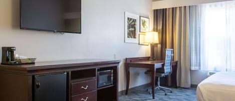 Una habitación de hotel con televisión de pantalla plana, un escritorio con silla, microondas, minibar y cama.