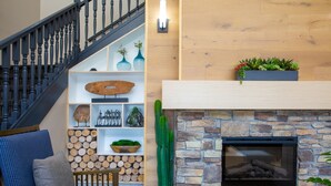 A staircase with a wooden railing, a seating area with a blue sofa and a wooden table, a wall with a stone fireplace, and a shelf with decorative items and plants. - Country Inn & Suites by Radisson, Tucson City Center, AZ (Tucson)
