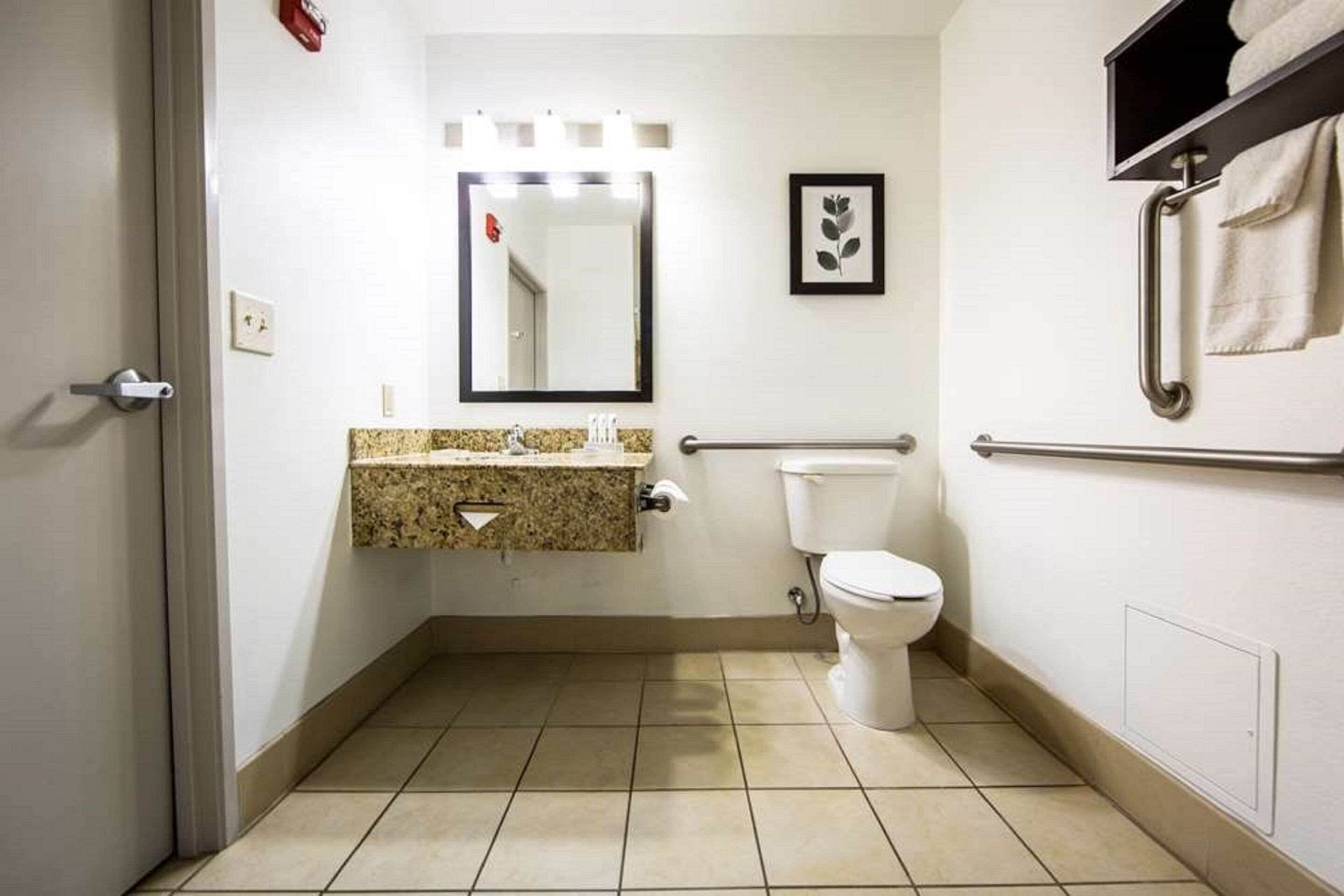 Un baño pequeño con inodoro, lavamanos de encimera de granito, espejo y barra para toallas.