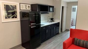 A modern kitchen with a black Galanz refrigerator, a microwave, and a sink. There are framed pictures on the wall and a red couch in the living area.