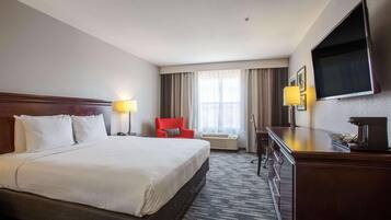 Une chambre d’hôtel avec un grand lit, un bureau doté d’un téléviseur à écran plat, un fauteuil rouge et une fenêtre avec des rideaux.