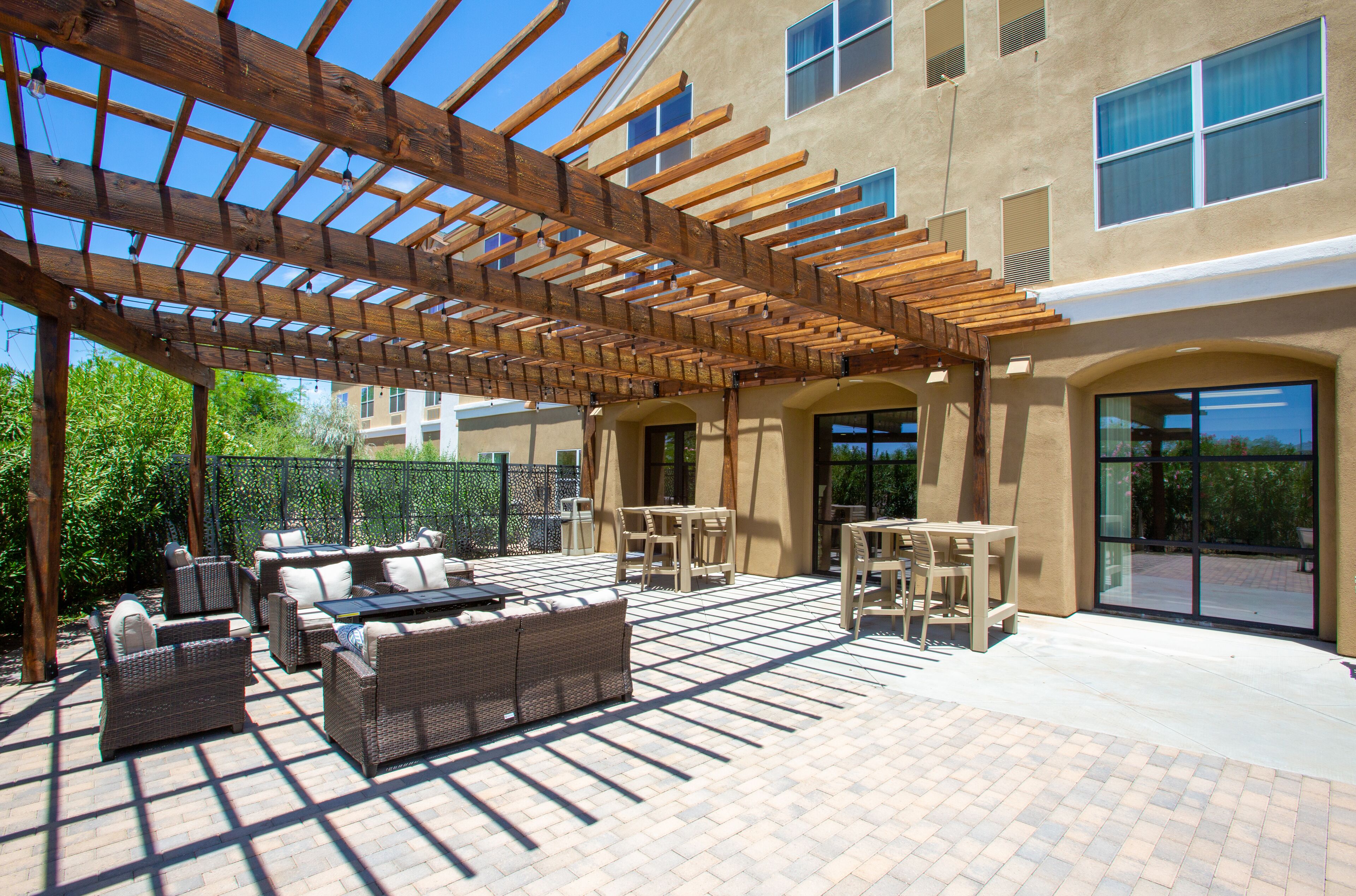 Une terrasse extérieure aménagée avec des meubles en osier, une pergola en bois et une vue sur un bâtiment doté de grandes fenêtres.