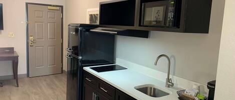 A compact kitchen with a built-in microwave, a stainless steel sink, and dark cabinetry.