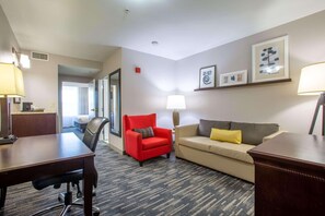 A hotel room with a wooden desk, a red armchair, a beige sofa, and a patterned carpet. - Country Inn & Suites by Radisson, Tucson City Center, AZ (Tucson)